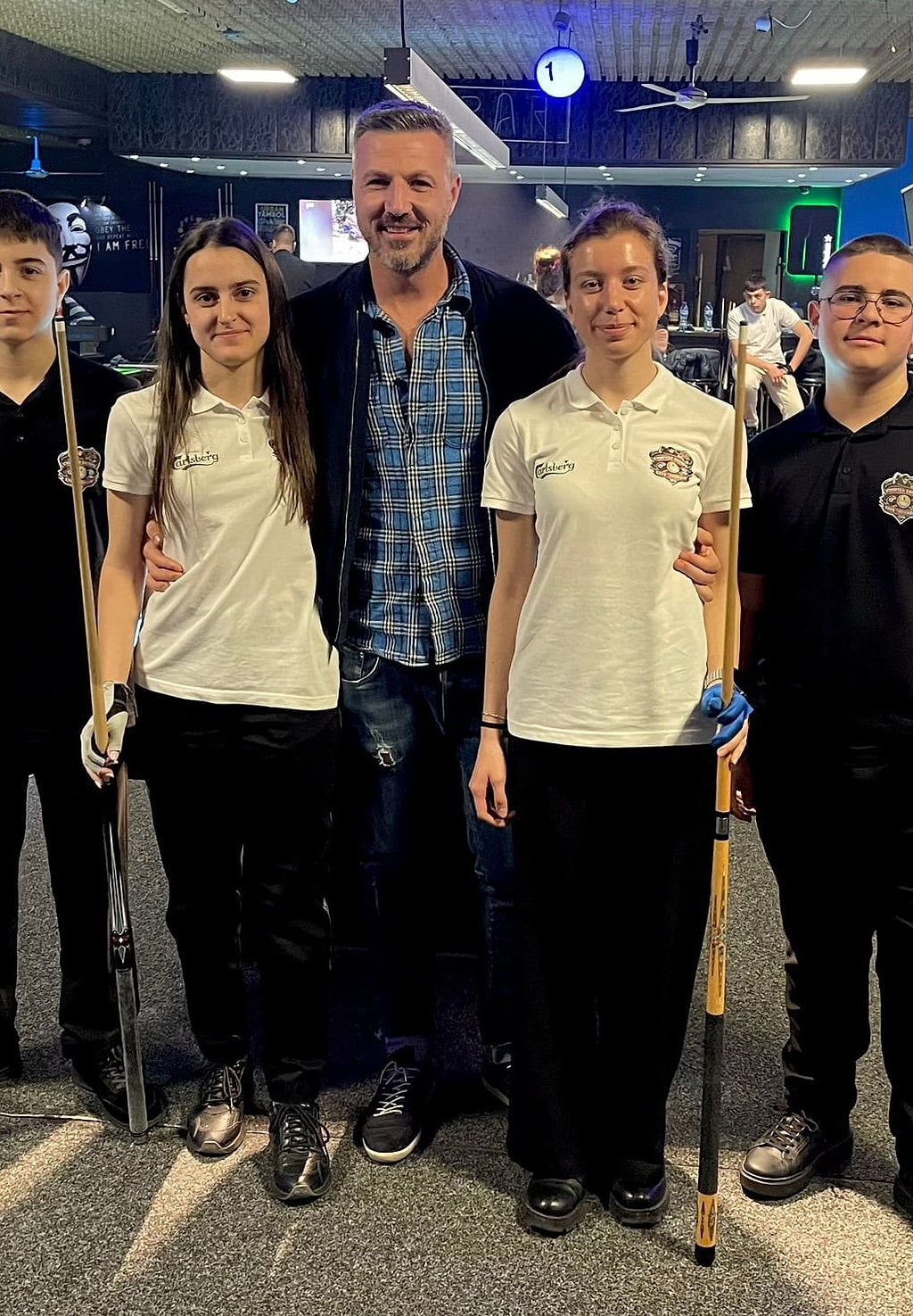 A coach with four academy students holding cues